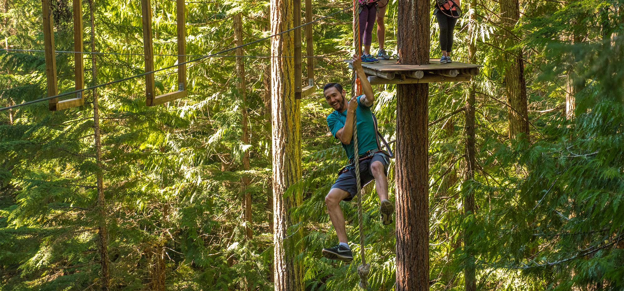 A climber crossing a rope obstacle high in the trees at the Whistler aerial obstacle course
