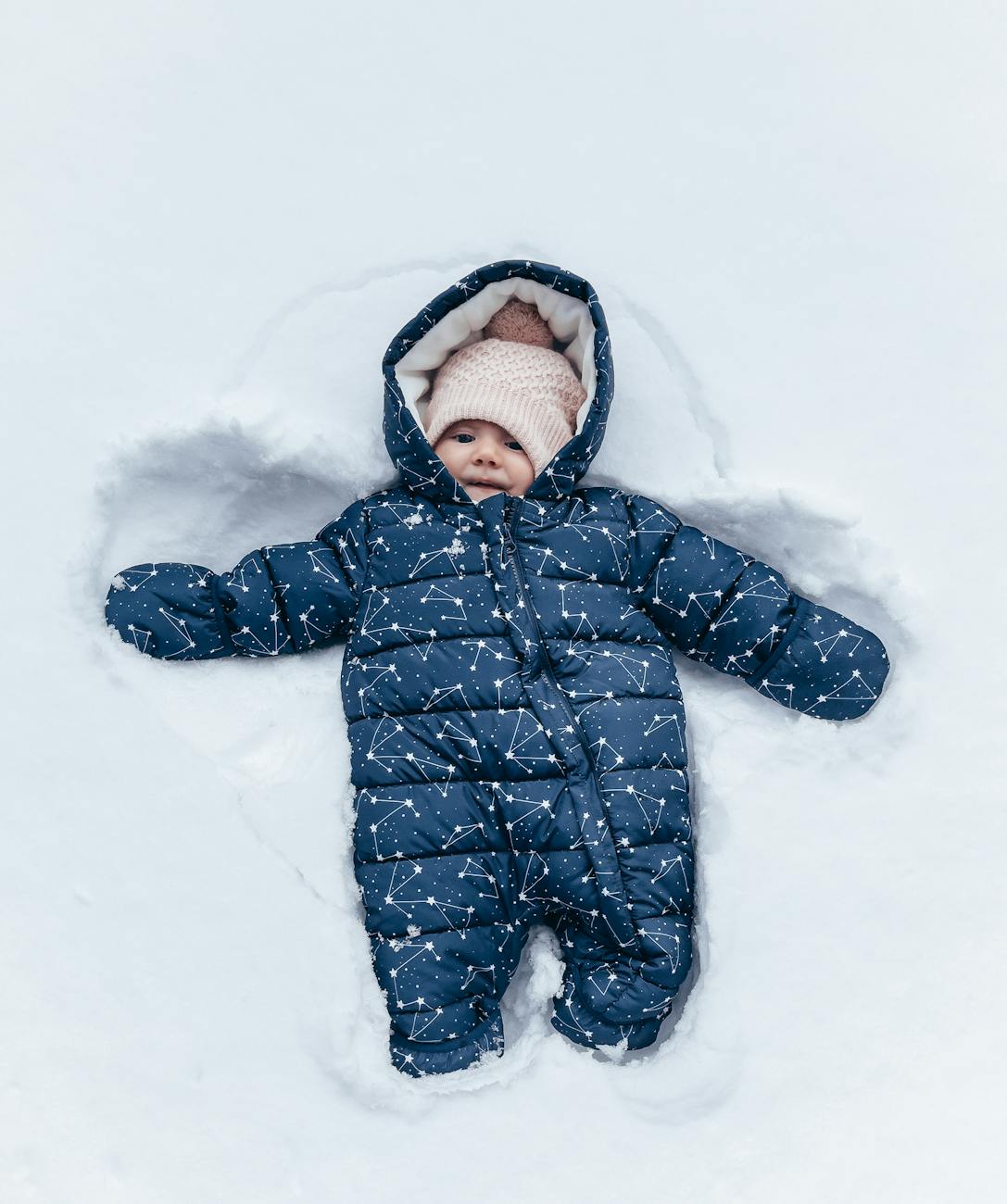 A baby in a navy snowsuit making a snow angel