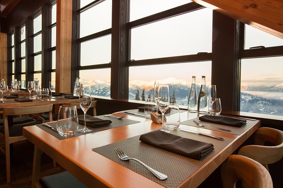 Tables set by the floor-to-ceiling windows at Christine's on Blackcomb at sunset