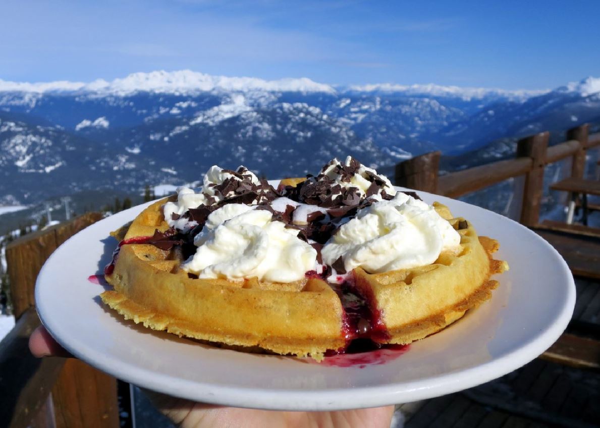 A Crystal Hut waffle loaded with berry compote and whipped cream, mountains behind