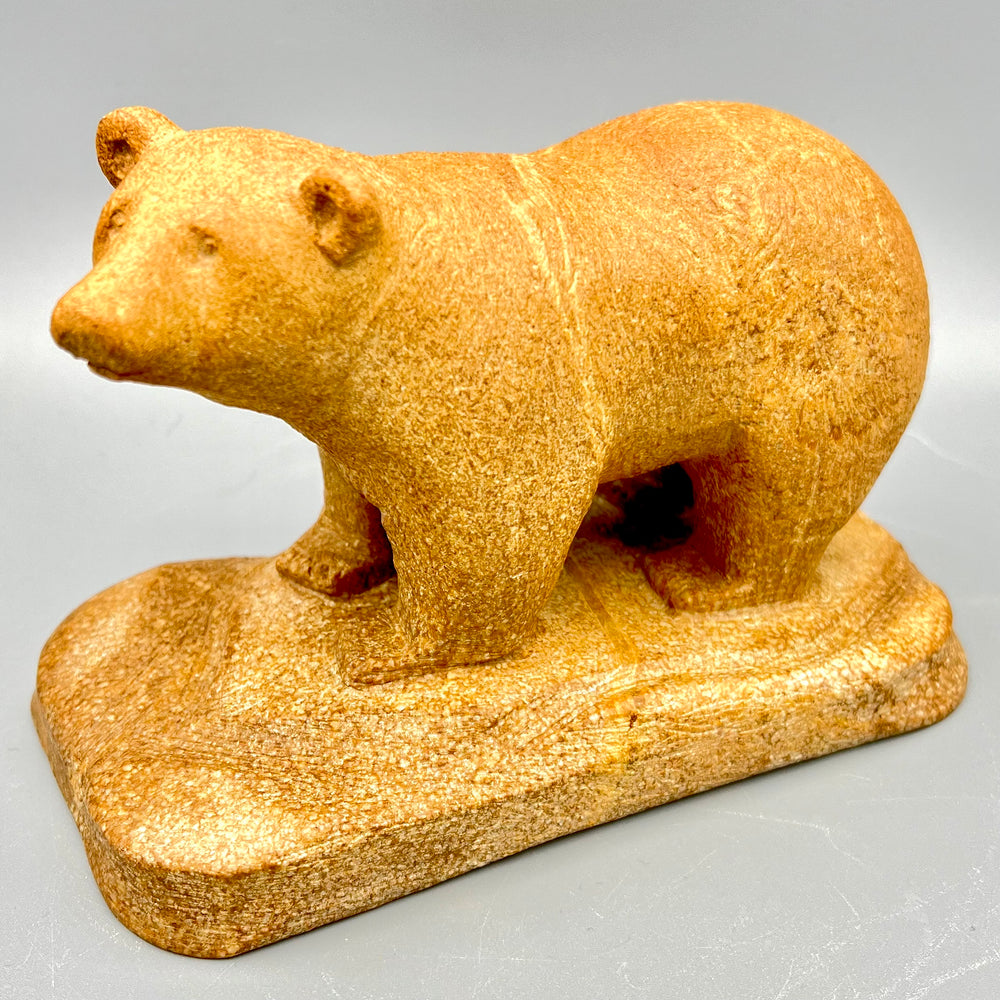 A golden soapstone bear sculpture standing on a stone base, carved in a longer class