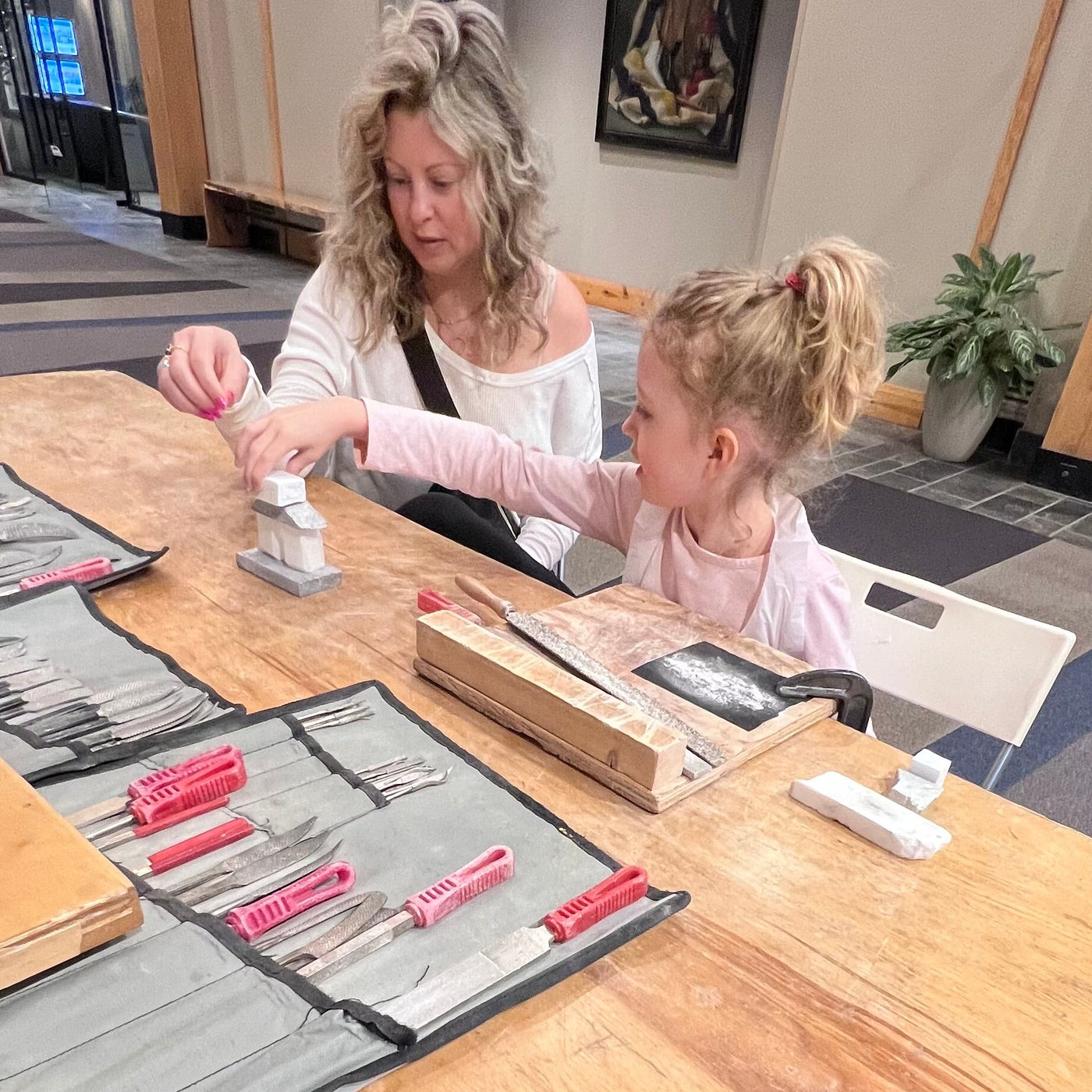 A parent and child carving a stone Inukshuk together at a workbench in the Fathom Stone Art studio