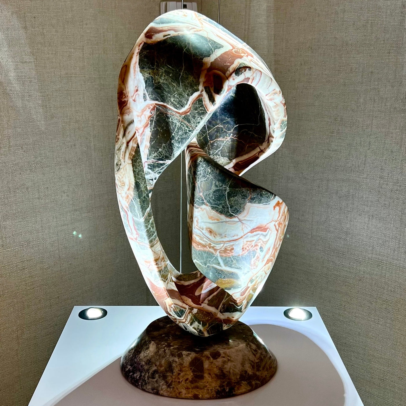 An abstract twisting onyx sculpture lit on a plinth in the gallery
