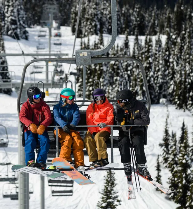 Skiers riding a chairlift above snowy forest at Whistler Blackcomb