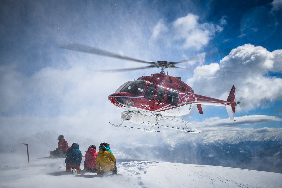 A helicopter landing beside a group of skiers on a snowy alpine ridge