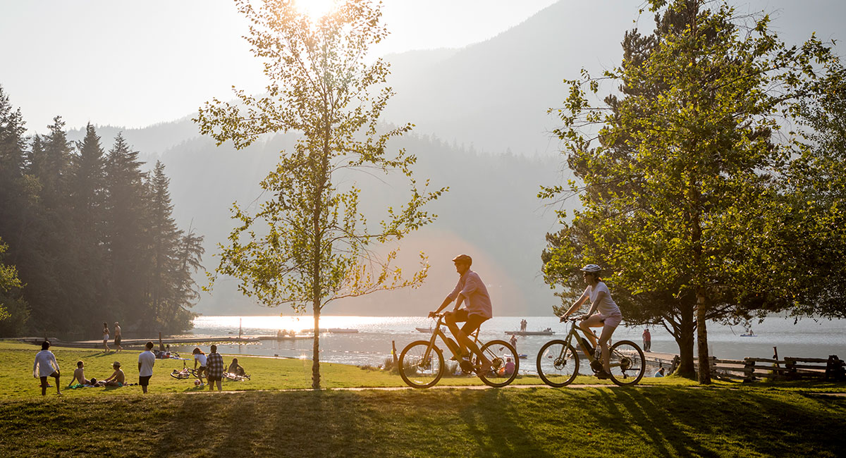 Two riders cycling through a lakeside park in Whistler at golden hour