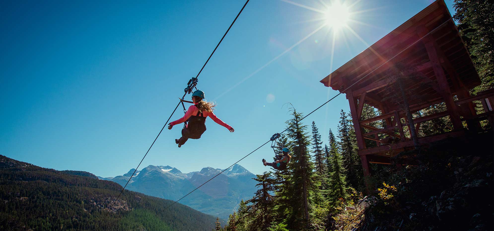 Two riders on parallel Superfly ziplines high above the forested valley on Cougar Mountain