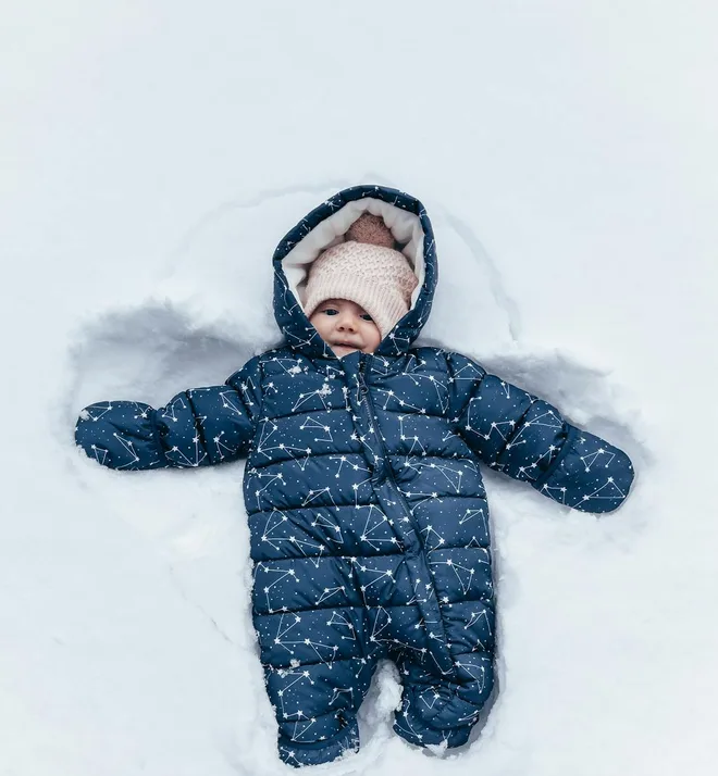A baby in a navy snowsuit making a snow angel