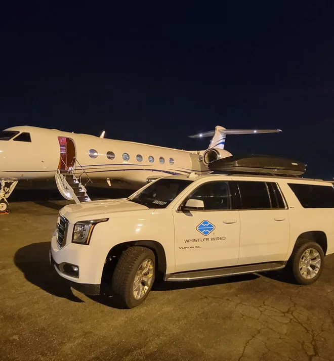 A Whistler Wired SUV waiting beside a private jet on the airport apron at night